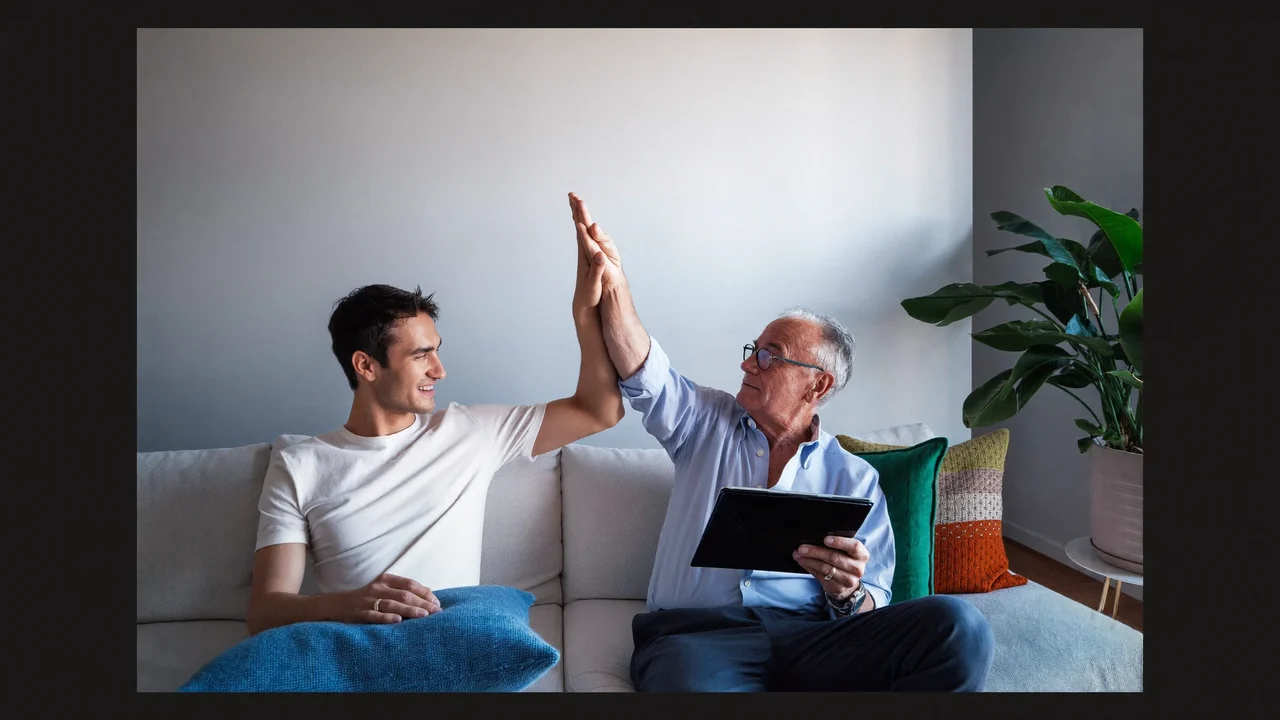Illustrazione: un adolescente e un nonno festeggiano insieme davanti a un tablet.